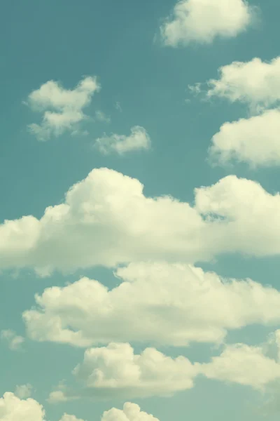 Blue sky, cloudy weather. Summertime landscape. Different size white clouds. Warm colors toned effect photography. Vertical