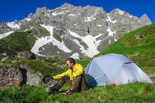 Mladý muž připravuje k jídlu na hořák u stanu v horách Gruzie — Stock fotografie