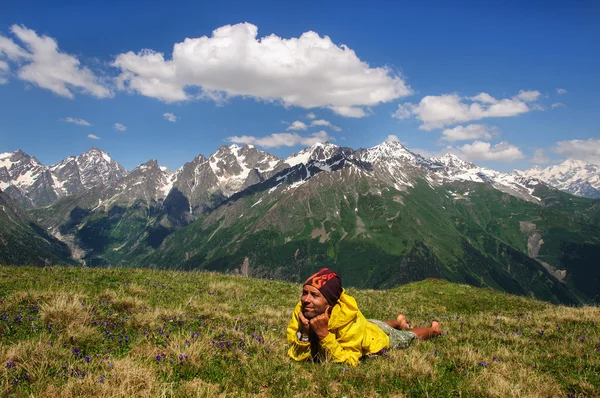 Man lying down resting on grass background of snow-capped peaks the mountains Georgia — Stock Photo, Image