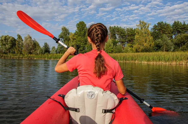 A young woman in bright clothes floats on a red kayak on the river. Ukraine