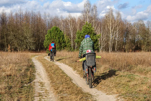 Dads ride their children in bicycle seats on a dirt road through the forest