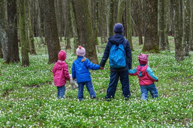 Mutlu çocuklar çiçek açan ormanda el ele yürürler.