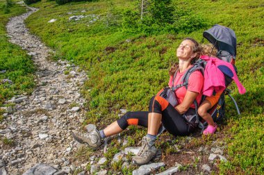Carpathian Gorgan 'da taştan bir yola tırmanmadan önce bir anne ve kızı taşıyıcı bir sırt çantasında çimlerin üzerinde dinleniyor. Ukrayna