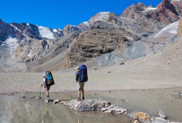 Un homme avec un sac à dos reposant sur un bâton de trekking déplace une rivière — Photo