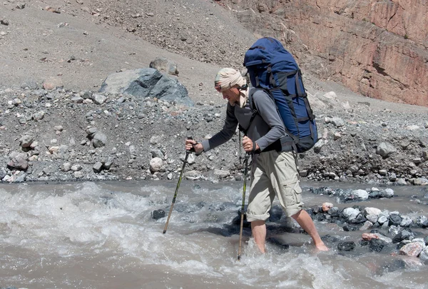Чоловік з рюкзаком відпочиває на пішохідному полюсі переміщує річку — стокове фото