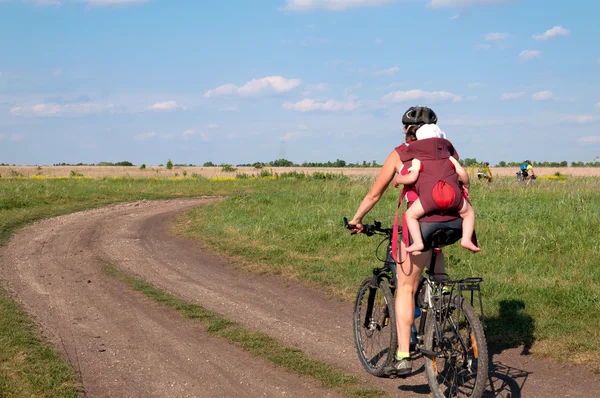 Ung mamma med hennes baby mountainbike rida på grusväg. — Stockfoto