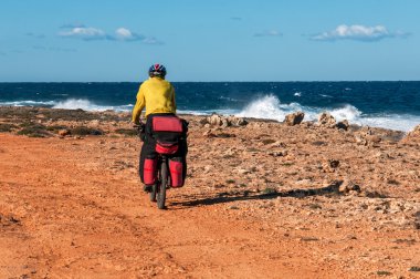 Adam dağ bisikleti büyük sırt çantası ile kumlu plaja gider.