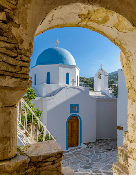 Традиционный кикладистский квартал с узкой улочкой, белыми домами и церковью с голубым куполом на греческом острове Лефкес Парос