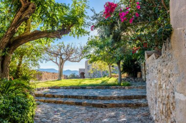 Monemvasia, Lakonia, Peloponnese, Yunanistan 'daki ortaçağ şatosunda dar taştan bir sokak ve renkli bir bougainvillea ile geleneksel mimari.