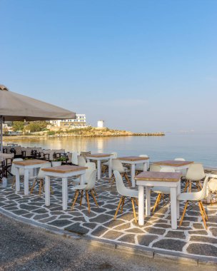 Plajın önündeki bir kafenin sabah manzarası ve Yunanistan 'ın Parikia Paros Körfezi' ndeki arka plan olarak geleneksel bir yel değirmeni.