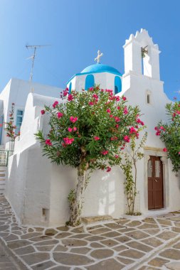 Traditional Cycladitic alley with a narrow street and a whitewashed church with a blue dome in Parikia, Paros island, Greece.