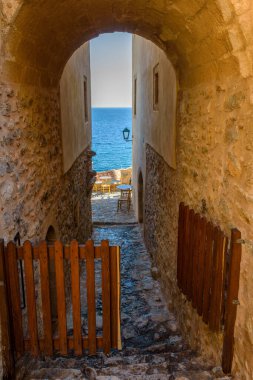 Monemvasia 'nın güçlendirilmiş ortaçağ şatosunda geleneksel bir kafe. Demir masalar ve arka planda Ege Denizi manzaralı ahşap sandalyeler.