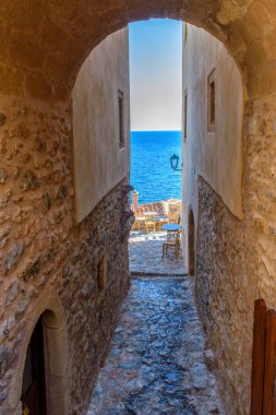 Monemvasia 'nın güçlendirilmiş ortaçağ şatosunda geleneksel bir kafe. Demir masalar ve arka planda Ege Denizi manzaralı ahşap sandalyeler.
