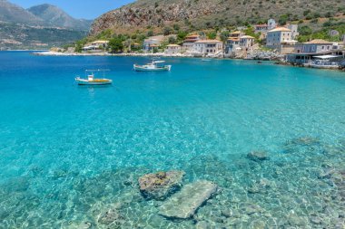 Limeni köyünün turkuaz sularda balıkçı tekneleri ve taştan binaların Mani, Güney Moreloponnese, Yunanistan 'da arka plan olarak kullanıldığı manzarası.