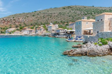 Limeni köyünün turkuaz sularda balıkçı tekneleri ve taştan binaların Mani, Güney Moreloponnese, Yunanistan 'da arka plan olarak kullanıldığı manzarası.