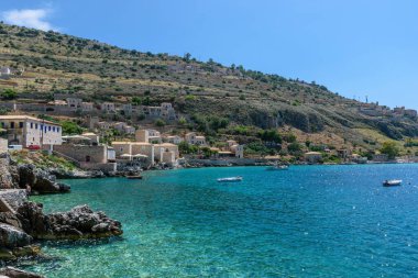 Limeni köyünün turkuaz sularda balıkçı tekneleri ve taştan binaların Mani, Güney Moreloponnese, Yunanistan 'da arka plan olarak kullanıldığı manzarası.