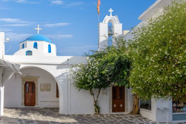 Traditional Cycladitic alley with a narrow street and a whitewashed church with a blue dome in Parikia, Paros island, Greece.