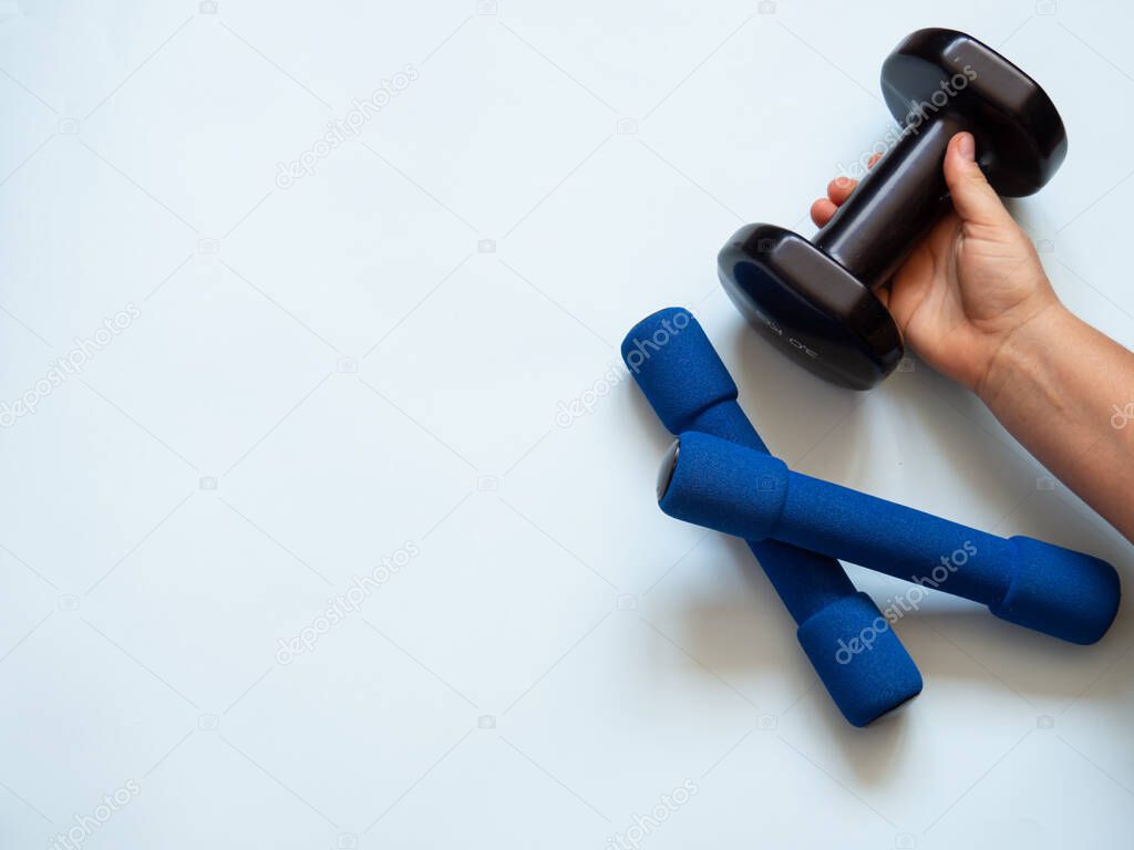Two blue small dumbbells and a caucasian woman hand grabbing one black dumbbell for weight and strength training in white background. Copy space for text. Weightlifting and healthy lifestyle concept