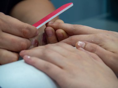 Güzellik salonunda manikür. Manikürcü bir profesyonelin tırnak törpüsü sırasında beyaz kadın elleri. Tırnaklar yakın. Güzellik uzmanı dosyasının bir müşteriye çivileri