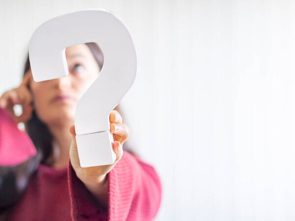 Question mark sign hold by a caucasian young woman with red sweater and thinking or confused expression. Communication, decision or response concept. Copy space.