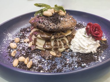 Çikolata fındık soslu krep, çökelmiş oreos, fıstık ve krem şanti. Siyah tabakta bir yığın krep. Lokantada pudra şekeri ve gül süslemesiyle servis edilen sağlıksız kahvaltı..