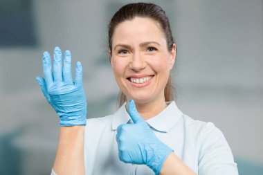 Kadın doktor ya da hemşire koruma için tıbbi eldivenlerini giyer ve baş parmağını kaldırır.