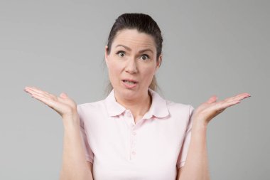 Orta yaşlı bir kadın omuz silker ve kollarıyla bir jest yapar. 