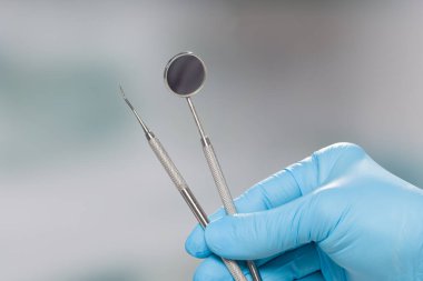 Diş hekiminin elini mavi eldivenlerle kapat. Muayene için kullanılan bir çift diş aletini göster.