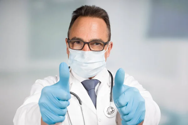 Mužský Lékař Laboratorním Plášti Obličejovou Maskou Stetoskopem Ukazuje Dvojité Palce — Stock fotografie
