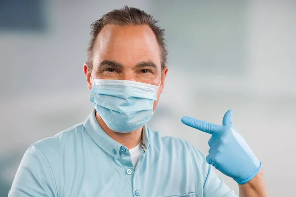 Doctor with medical face mask and medical gloves is pointing to his mask