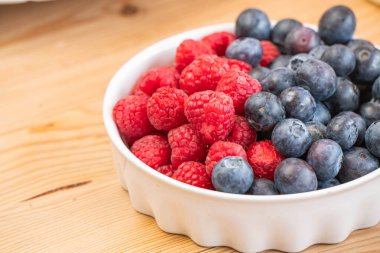 Ahşap kasede taze meyveler (çilek, ahududu, yabanmersini, kivi, mango)