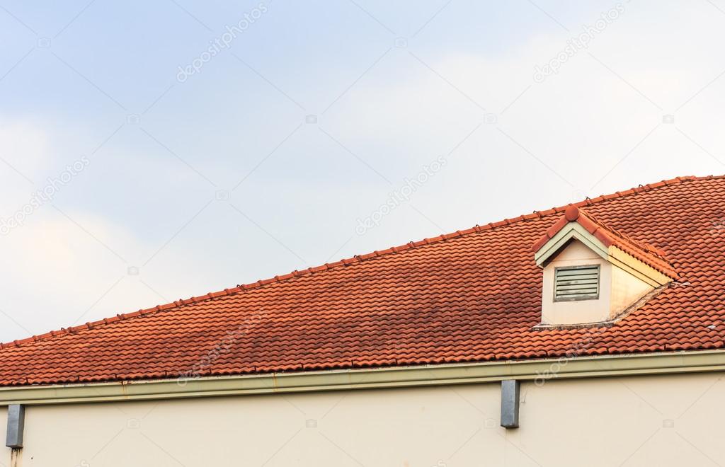 Chimneys on roof of red tiles with blue sky and clouds.