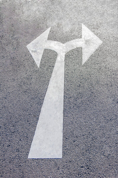 A two way arrow symbol on a black asphalt road surface.
