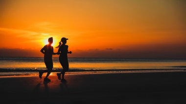 Young couple: man and woman run together on a sunset on lake coa clipart
