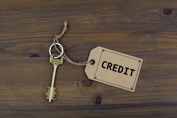 Key and a note on a wooden table with text - Credit — Stock Photo, Image