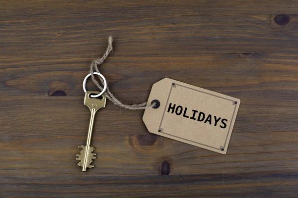 Key and a note on a wooden table with text - Holidays — Stock Photo, Image