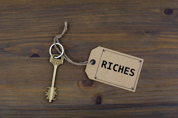 Key and a note on a wooden table with text - Riches — Stock Photo, Image