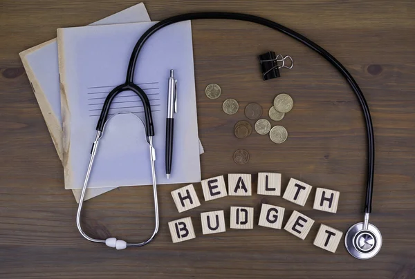 Stetoscopio, denaro, penna con taccuino e testo: Bilancio sanitario — Foto Stock