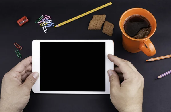 Manos de un hombre sosteniendo un dispositivo de tableta en blanco sobre un espacio de trabajo negro — Foto de Stock