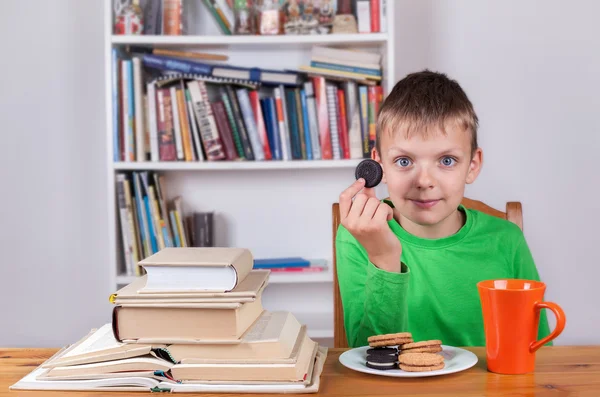Chłopiec siedzi przy stole i i jedzenia ciastka — Zdjęcie stockowe
