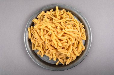 Strozzapreti, gri bir masada metal tabakta İtalyan makarnası.