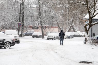 Şehir ortamında kar yağışı ve don. Arabalar ve binalar karla kaplı.