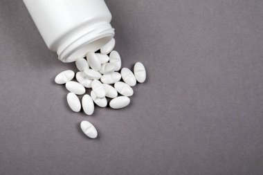 Beyaz ilaç kutusu ve gri arka planda haplar.