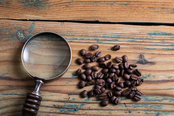 Coffee beans and a magnifying glass on a wooden table. Research and search concept — Stock Photo, Image