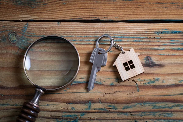 Property key and magnifying glass on wooden table. Market research, supply and demand concept