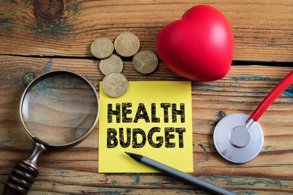 Orçamento de Saúde. Coração de borracha, dinheiro, lápis e lupa em um fundo de madeira — Fotografia de Stock