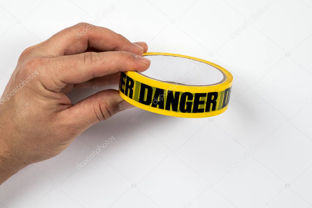 DANGER, yellow warning tape in a mans hands on a white background