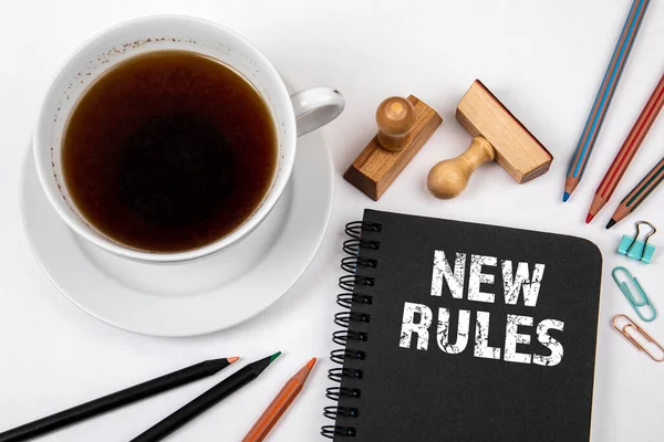 Νέοι κανόνες. Μαύρο σημειωματάριο, φλιτζάνι καφέ και είδη γραφείου σε λευκό τραπέζι — Φωτογραφία Αρχείου