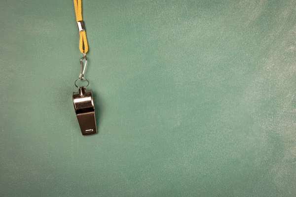 Assobio de metal com cabo amarelo em uma placa de giz verde — Fotografia de Stock