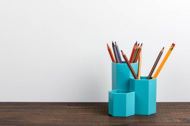 Ahşap bir masa ve beyaz bir arka plan üzerinde renkli kalemleri olan tutucu